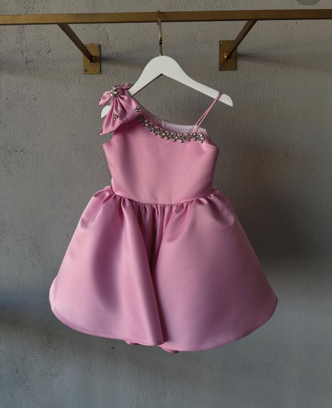 Pink dress with embellishments on a hanger against a plain wall